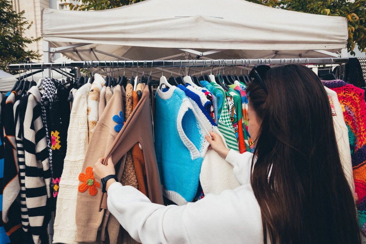 Shopper flicking through a densely packed rail of vintage clothing at a market stall